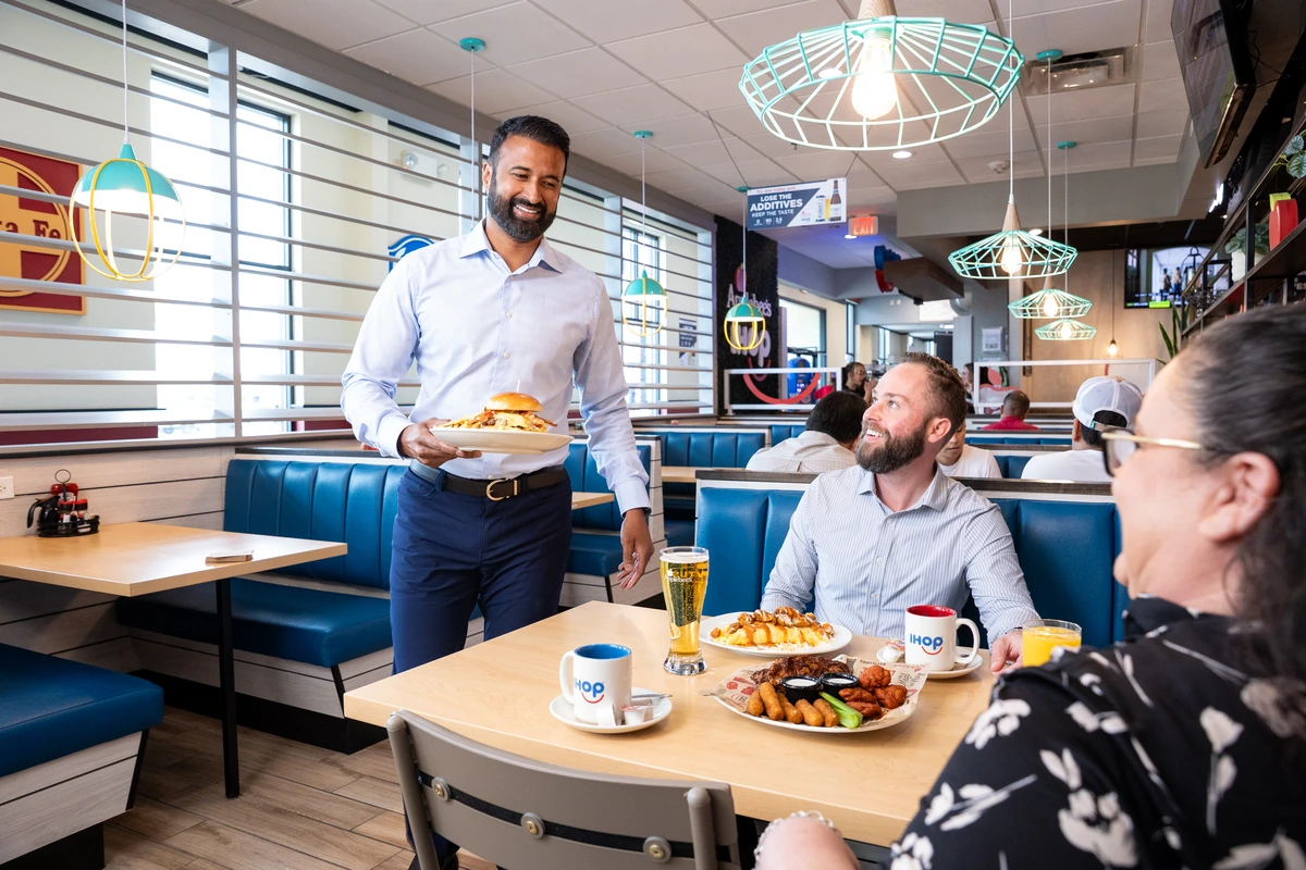 Alex Anthraper serving a meal to guests at a restaurant table