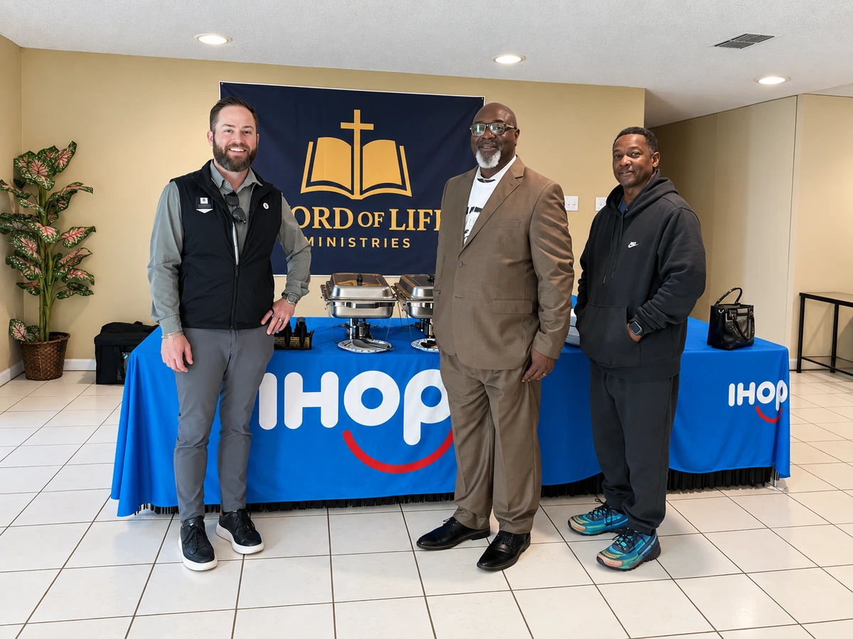 Three community partners standing beside an IHOP table at Word of Life Ministries
